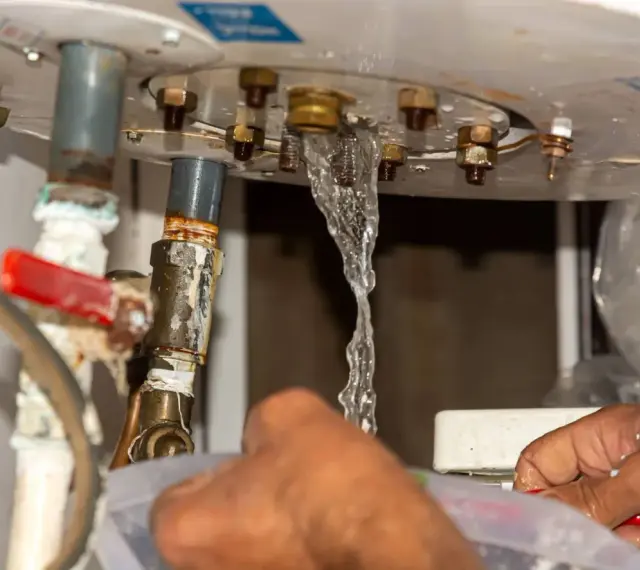 Fuite d'eau par le haut du chauffe-eau, un danger potentiel. Les mains tentent de contenir le liquide.