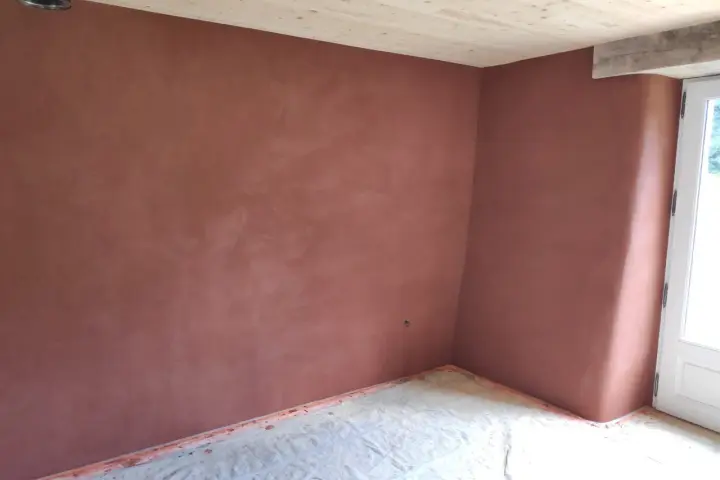 Un coin de pièce aux murs recouverts d'un enduit chaux sable ocre. Le sol est protégé par une bâche. Le plafond est en bois clair.