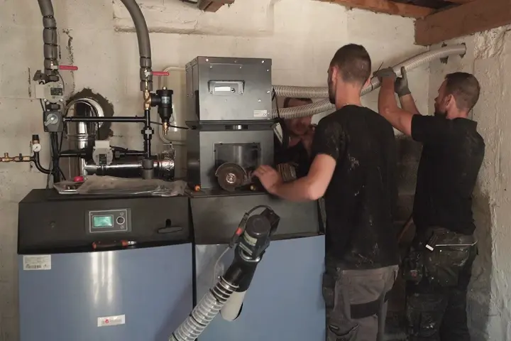 Techniciens installant une nouvelle chaudière, remplaçant une ancienne chaudière fioul. Travaux de chauffage en cours.
