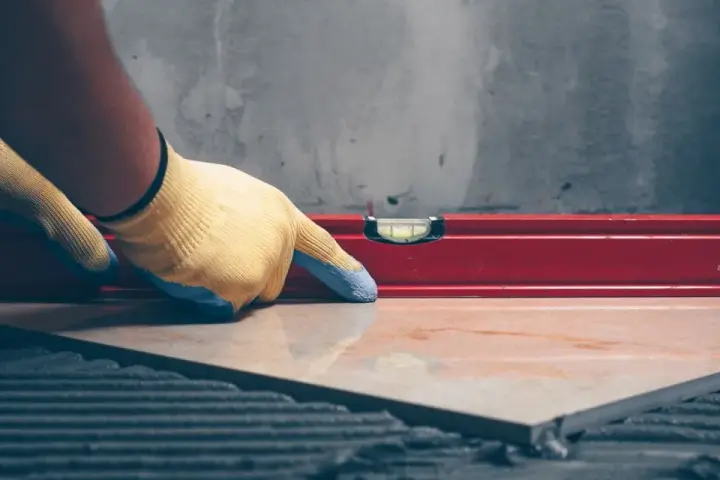 Pose d'un carrelage avec un niveau à bulle pour vérifier l'épaisseur du carrelage et de la colle.