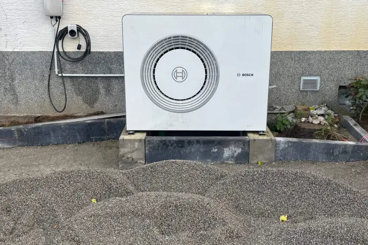 Unité extérieure d'une chaudière à condensation Bosch, installée sur des blocs de béton, avec un chargeur mural à proximité.