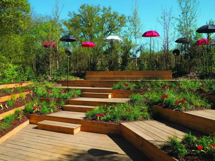 Un jardin aménagé avec des terrasses en bois et une **profondeur marche escalier extérieur** sur plusieurs niveaux, décoré de tulipes rouges et de parasols colorés.