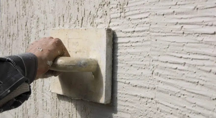 Main d'un artisan appliquant un enduit projeté texturé. Le prix au m2 de ce type de finition est souvent demandé.