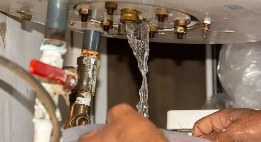 Fuite d'eau par le haut du chauffe-eau, près d'un joint rouge. Un filet d'eau s'échappe des raccords métalliques.