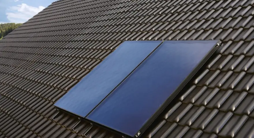 Deux panneaux de chauffage solaire thermique installés sur un toit en tuiles sombres, sous un ciel bleu.