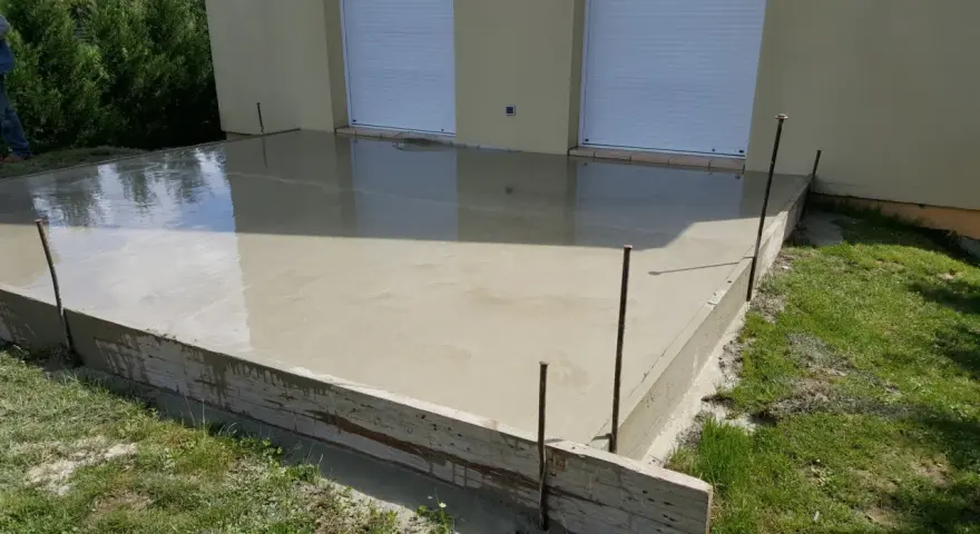 Dalle en béton fraîchement coulée pour une maison, avec coffrage en bois et ferraillage apparent. L'épaisseur de la dalle est visible.