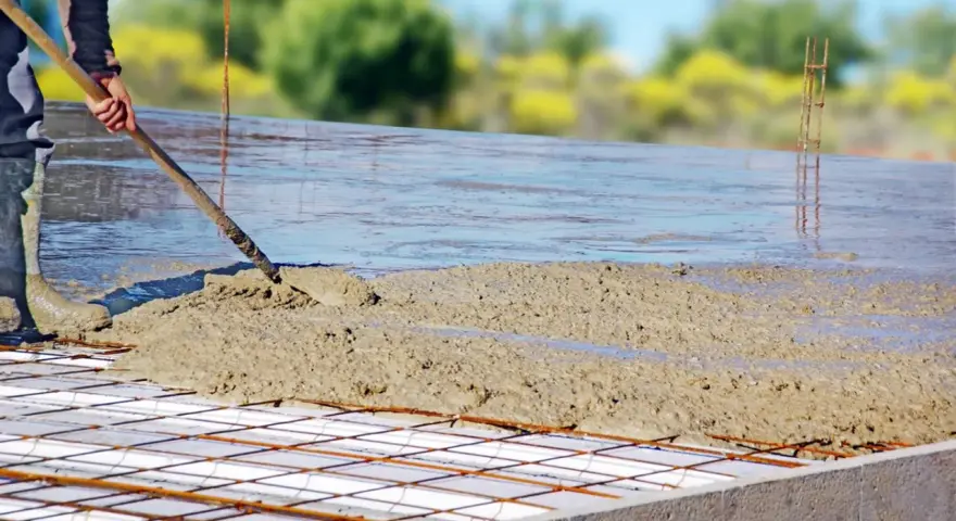 Coulée de béton frais sur une armature métallique pour assurer l'épaisseur dalle maison. Le travailleur étale le béton avec une pelle.