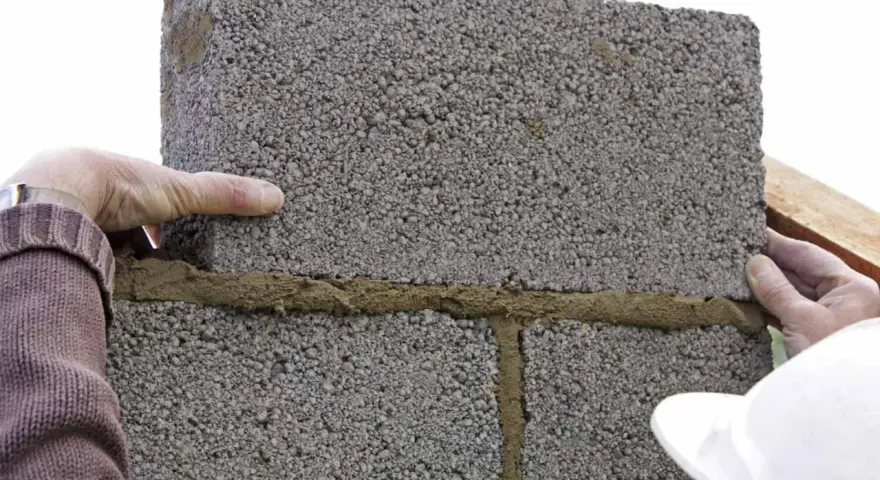 Pose de parpaings avec mortier. On voit les mains d'un maçon ajustant une brique. La question est : combien de mortier pour 1m2 de parpaing ?