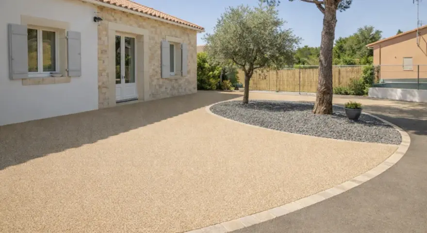 Allée de maison avec béton désactivé de belle épaisseur, bordée de pierres et de gravier sombre autour d'un arbre.