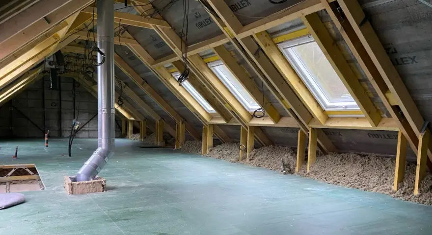 Aménagement des combles d'une maison Phénix : charpente, fenêtres de toit, isolation et gaine de ventilation en cours.