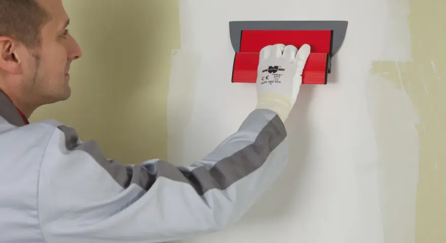 Un ouvrier utilise un outil pour appliquer une bande de placo sur un mur.