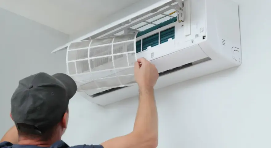 Un homme retire un filtre à air sale d'une unité de climatisation murale, étape essentielle de l'entretien climatisation maison pour un air sain.
