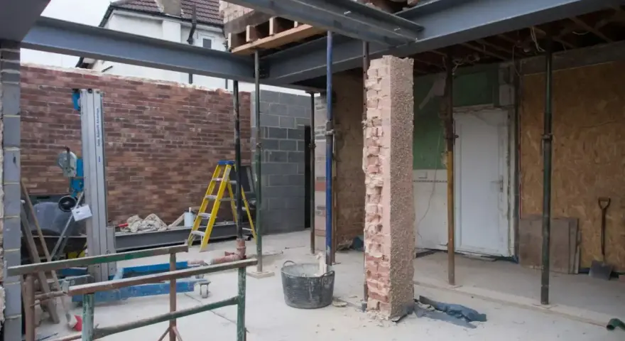 Travaux de rénovation : agrandir ouverture mur porteur avec poutres métalliques. Échafaudages, briques et outils sur le chantier.