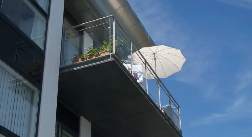 Balcon en béton moderne, prêt pour une rénovation. Des plantes en pot et un parasol blanc attendent le soleil.