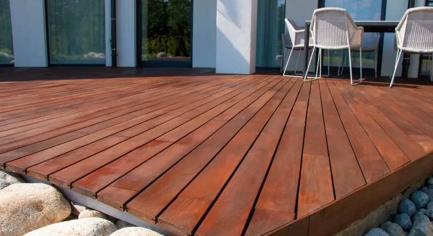 Belle terrasse en bois sur plot, avec des meubles de jardin et des rochers.