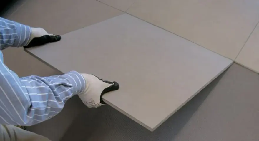 Pose d'une nouvelle dalle pour coller du carrelage sur du carrelage. Les mains gantées ajustent la pièce sur le sol existant.