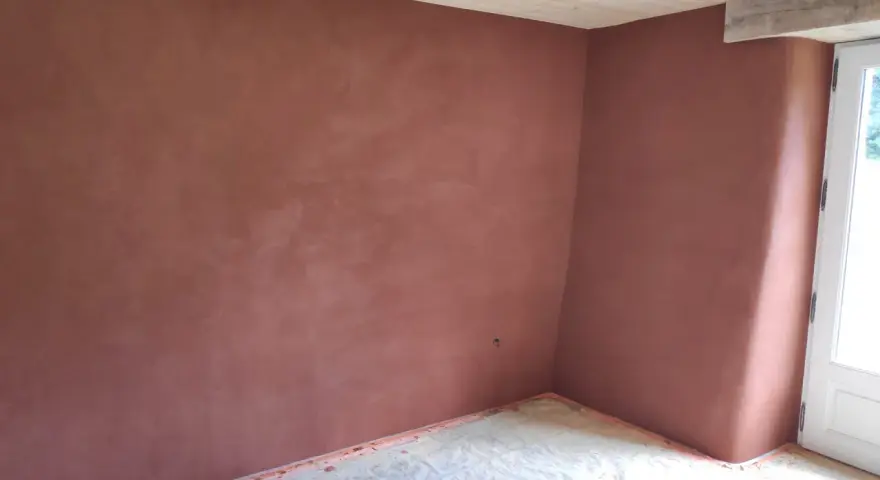 Un coin de pièce aux murs recouverts d'un enduit chaux sable ocre. Le sol est protégé par une bâche. Le plafond est en bois clair.