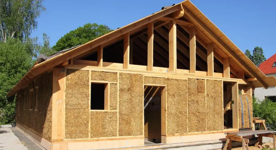 Construction d'une maison en paille écologique, avec une structure en bois visible et des murs isolés en bottes de paille.