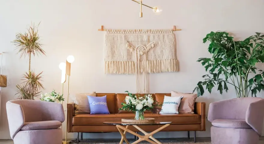 Salon moderne avec canapé en cuir marron, fauteuils roses poudrés, tapis texturé et macramé mural. La couleur peinture salon est neutre, mettant en valeur les meubles.