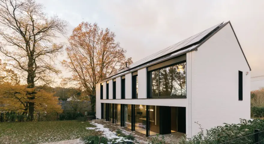 Agrandissement maison ossature bois moderne avec panneaux solaires, entourée d'arbres aux couleurs d'automne et d'un jardin enneigé.