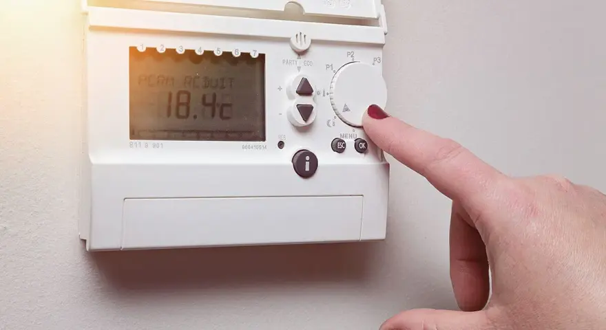Main d'une femme ajustant un cee thermostat connecté affichant 18.4°C.