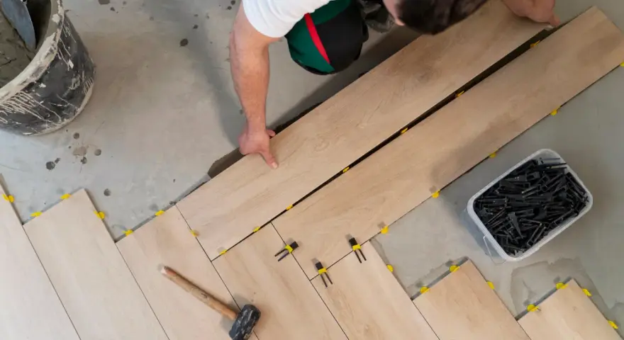 Pose d'un carrelage imitation bois sur un plancher. Un ouvrier pose les lames, des cales jaunes et noires assurent l'espacement.