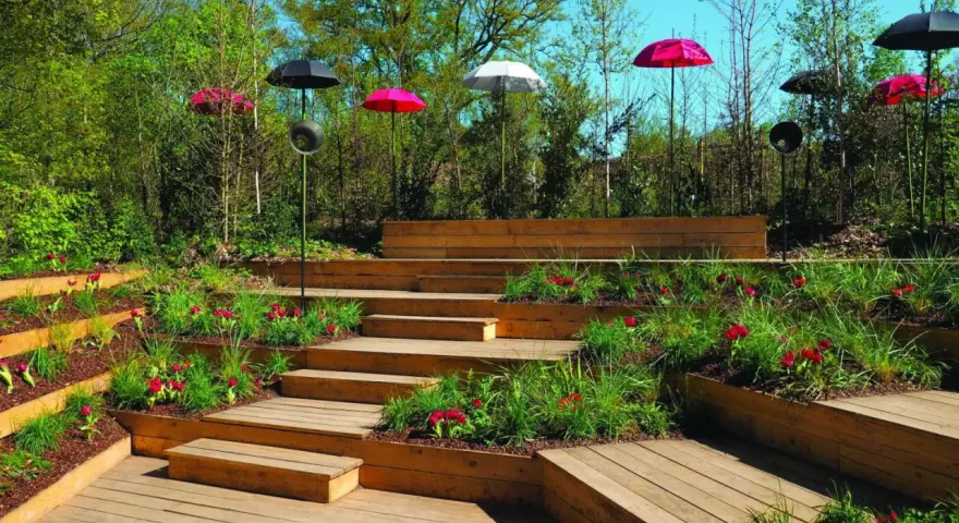 Un jardin aménagé avec des terrasses en bois et une **profondeur marche escalier extérieur** sur plusieurs niveaux, décoré de tulipes rouges et de parasols colorés.