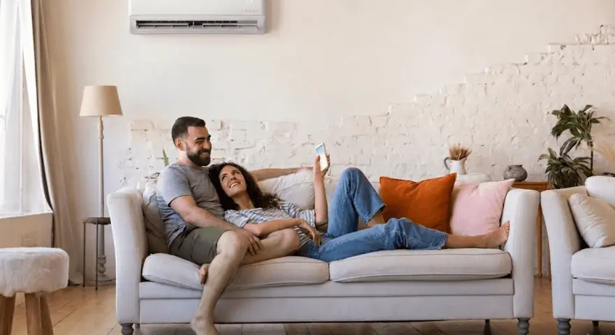 Couple détendu sur un canapé, profitant du confort d'une climatisation réversible. Aide EDF pour un intérieur agréable.
