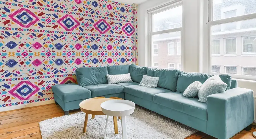 Un salon moderne avec un canapé bleu sarcelle et un papier peint intissé aux motifs ethniques colorés.