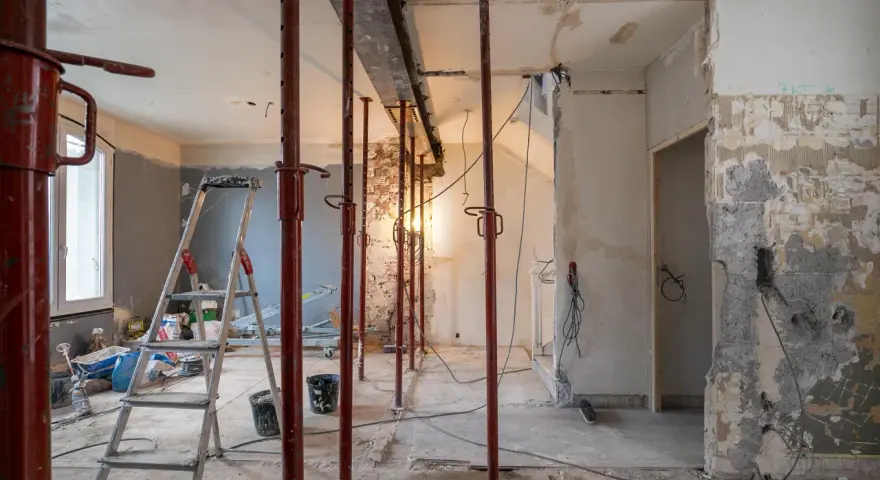 Chantier en cours : étais rouges soutenant un linteau, murs abattus, échelle et matériaux. Préparation pour une ouverture mur porteur.