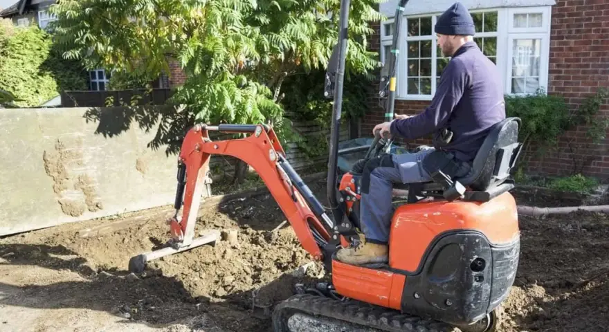 Un ouvrier manœuvre une mini-pelle orange pour des travaux de terrassement. Le prix du terrassement au m2 est une préoccupation pour ce chantier.