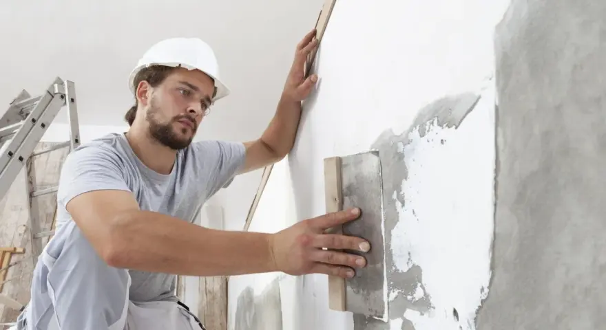 Artisan appliquant un enduit sur béton intérieur, préparant le mur pour une finition parfaite.