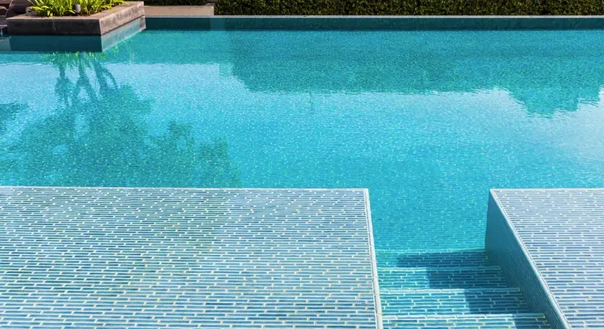 Élégante rénovation piscine mosaïque bleue, avec des marches carrelées et une végétation luxuriante.