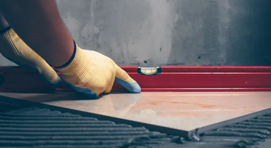 Pose d'un carrelage avec un niveau à bulle pour vérifier l'épaisseur du carrelage et de la colle.