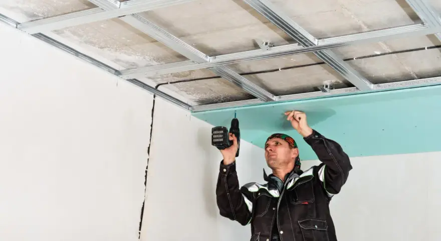 Un ouvrier réalise le schema montage placo plafond, fixant une plaque verte sur une structure métallique.