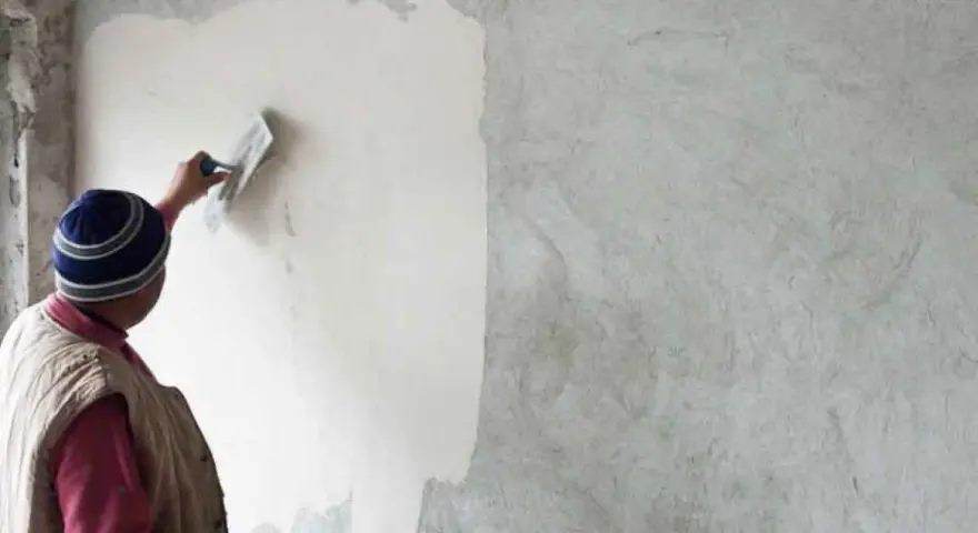 Un artisan applique un enduit chaux sable intérieur sur un mur avec une truelle. La texture naturelle du mortier est visible.