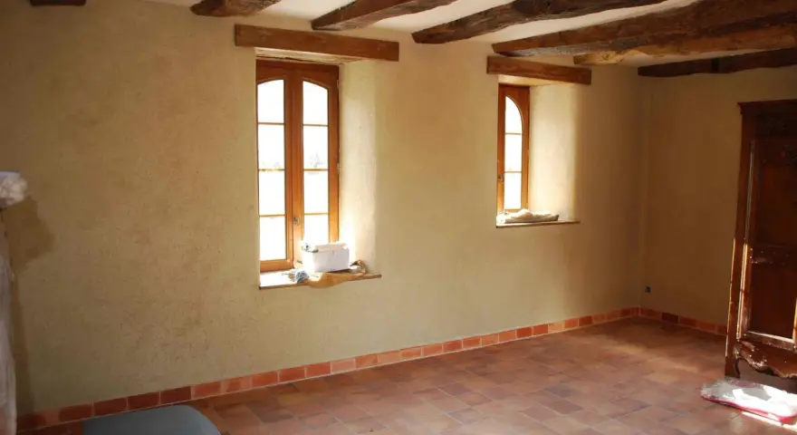 Intérieur d'une pièce aux poutres apparentes, murs en chaux chanvre pour une isolation naturelle, sol carrelé.