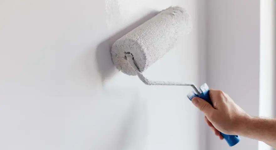 Main d'homme appliquant de la peinture blanche sur un mur avec un rouleau. Un guide visuel pour comment peindre un mur.