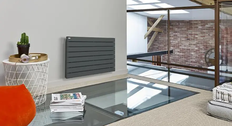 Radiateur réversible sans pompe à chaleur, gris anthracite, monté sur un mur blanc. Un cactus et des écouteurs sur une table d'appoint.