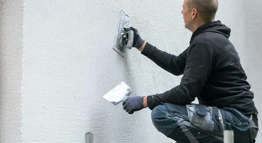 Un ouvrier applique un enduit sur un mur extérieur avec une truelle.