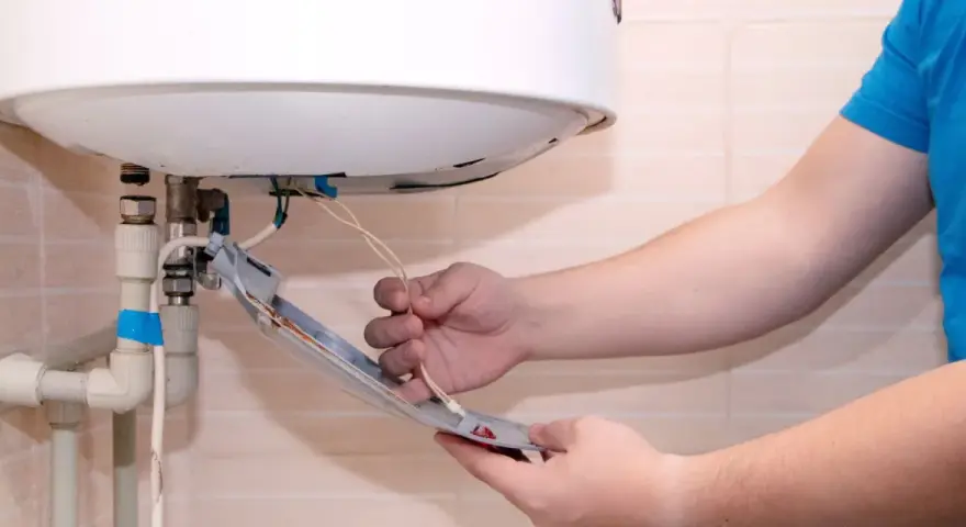Main tenant vérifie son chauffe eau qui fait disjoncter. Il tient une pièce détachée avec des fils électriques.