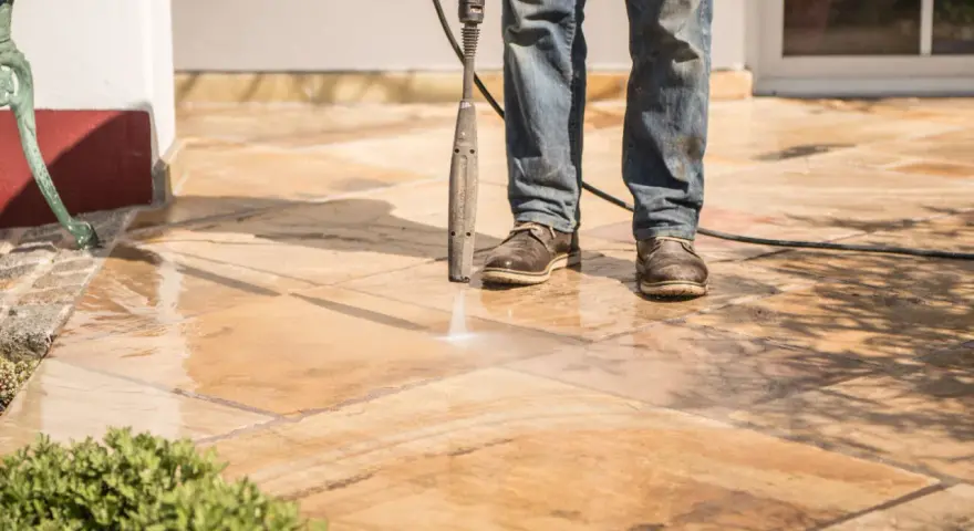 Nettoyer carrelage extérieur noirci avec un nettoyeur haute pression. L'eau projetée révèle la beauté naturelle des dalles.