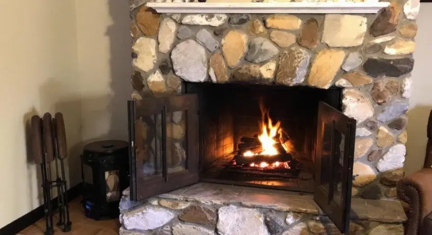 Un feu crépite dans une cheminée en pierres. Quel parement derrière poêle à bois, avec des accessoires de cheminée à gauche.