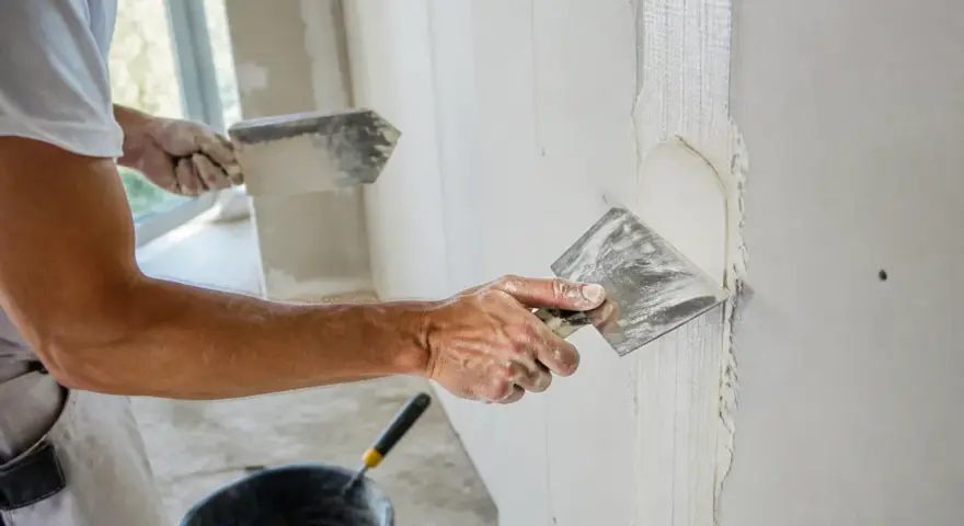 Un ouvrier applique de l'enduit sur une bande de placo. La question "faut-il humidifier les bandes placo" est au cœur de ce travail de finition.