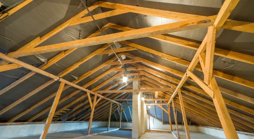 Charpente de grenier en bois, avec une bâche noire recouvrant le toit, suggérant une isolation rampant par l'intérieur en cours.