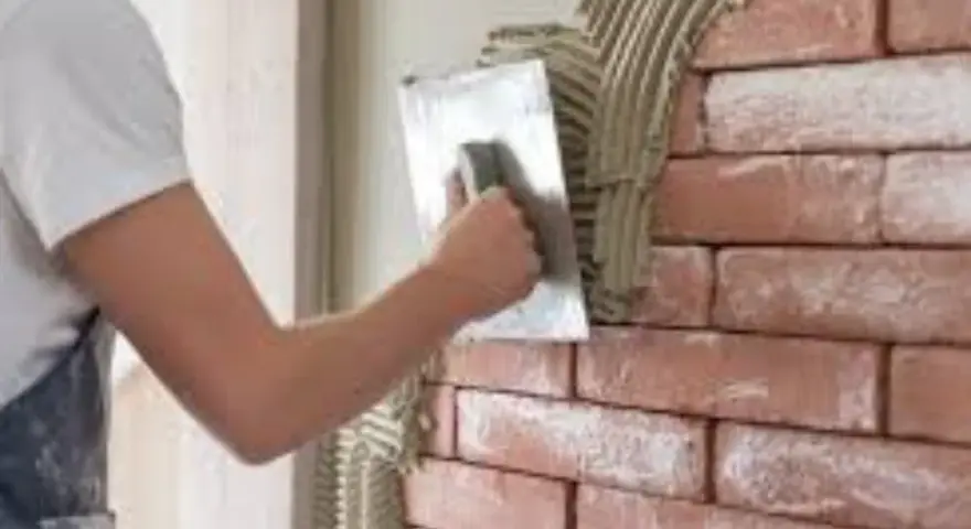 Un ouvrier applique de l'enduit sur une brique avec une truelle, créant une texture rustique.