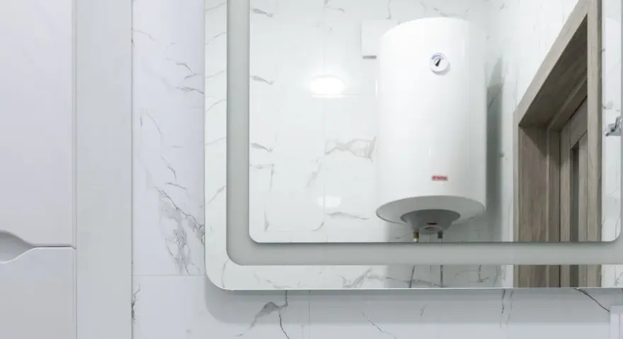 Gros chauffe-eau blanc, une chaudière micro accumulation, reflété dans un grand miroir, sur fond de carrelage marbré.