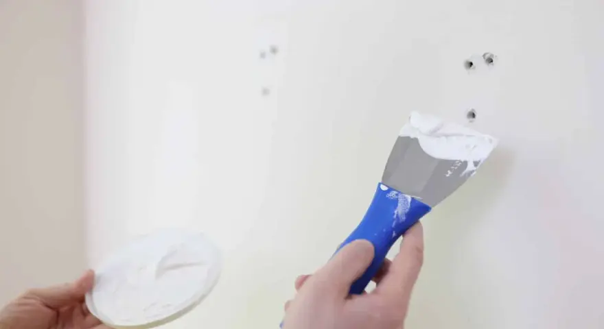 Main tenant en main une spatule chargée de mastic, prêt à reboucher trou mur.