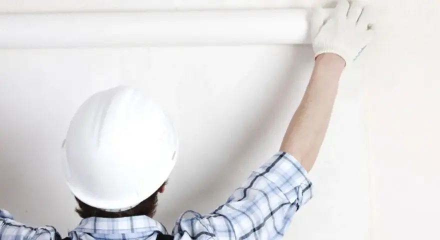 Un ouvrier en casque blanc déroule une **pose toile de verre** sur un mur blanc.