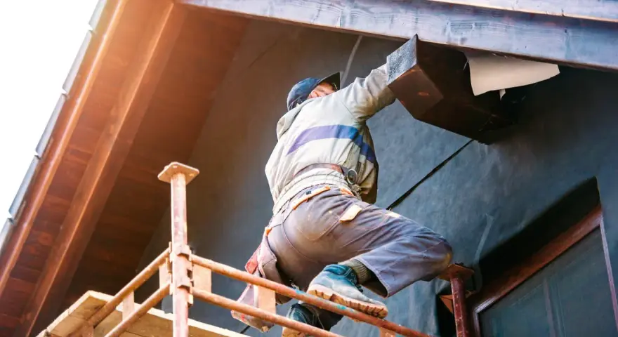 Un ouvrier sur un échafaudage installe l'isolation extérieur facade d'une maison, protégeant la structure en bois.